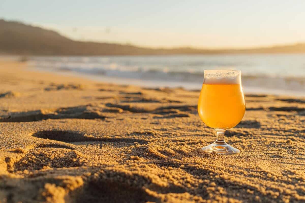 Great Ocean Road Breweries Cover Image with a Pint of Beer in focus on the Sand next to the ocean 