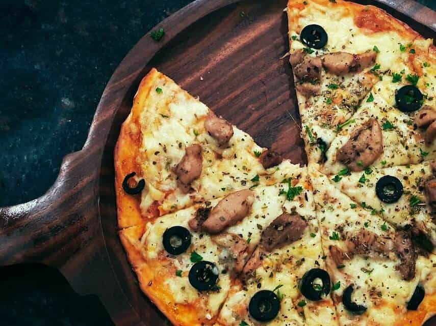 Pizza with a slice cut out on a circular wooden board on a black countertop