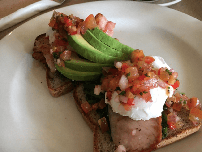 Toast topped with poached egg, bacon, avocado and bruschetta mix on a white plate at Sandy Feet Cafe Apollo Bay 