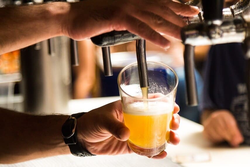 Close up shot of a mans hands holding a pint pot on an angle while dispensing beer from a pump