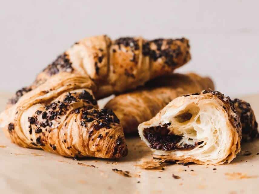 3 Croissants stacked on a beige piece of paper with one ripped in half facing the camera with chocolate inside