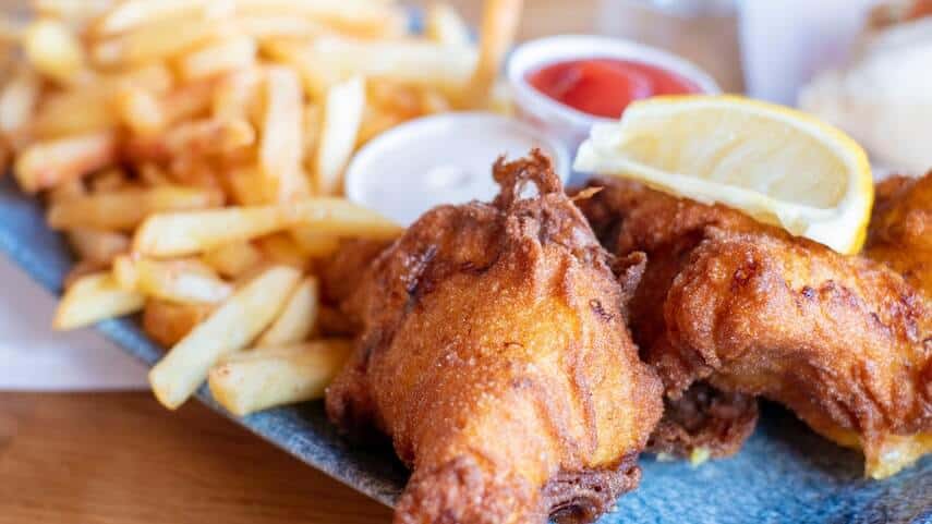 Fish and Chips on a plate topped with a slice of lemon with a small pot of tomato sauce between the fish and chips