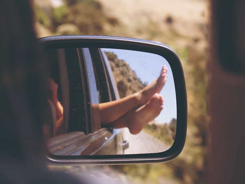 Photo of the wing mirror of of car reflecting legs crosses out of the window